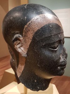Kopf einer Statue aus schwarzem Stein mit rotem Streifen.