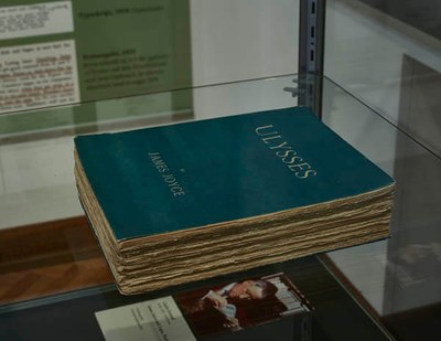 In einer Vitrine liegt ein grün-blaues gebundenes Buch. Es handelt sich um Ulysses von James Joyce.