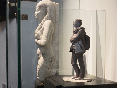 Kleine Skulptur eines modernen Menschen vor einer großen antiken Statue aus weißem Stein.