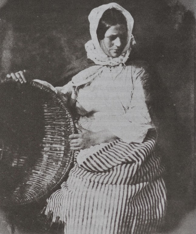 Schwarzweißfoto einer Frau in traditioneller Kleidung mit einem großen Korb.