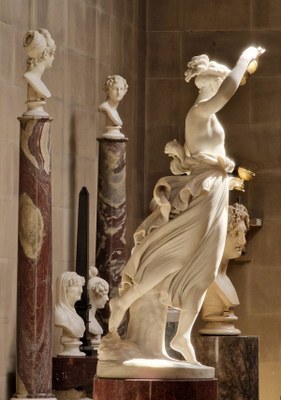 Eine weiße Frauenstatue neben vielen weißen Büsten auf Säulen und Podesten aus rotem Marmor.