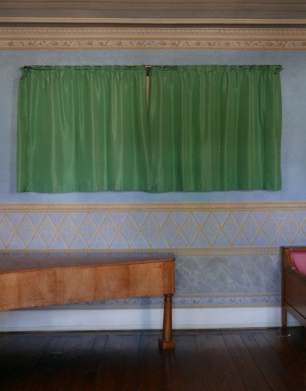 Grüner zugezogener Vorhang an einer hellblauen Wand mit goldenen Details. Darunter steht ein braunes Klavier.