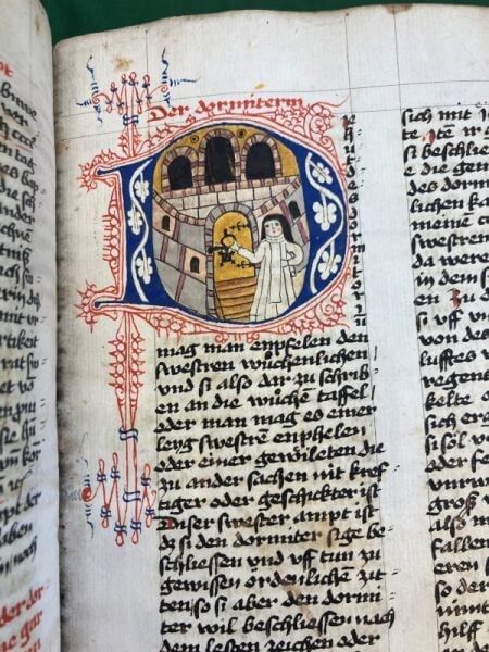 Alte Buchseite mit schwarzer, verschnörkelter, handgeschriebener Schrift und einer farbigen Miniaturmalerei einer bleichen frau in weißen Gewändern vor einer goldenen Tür.
