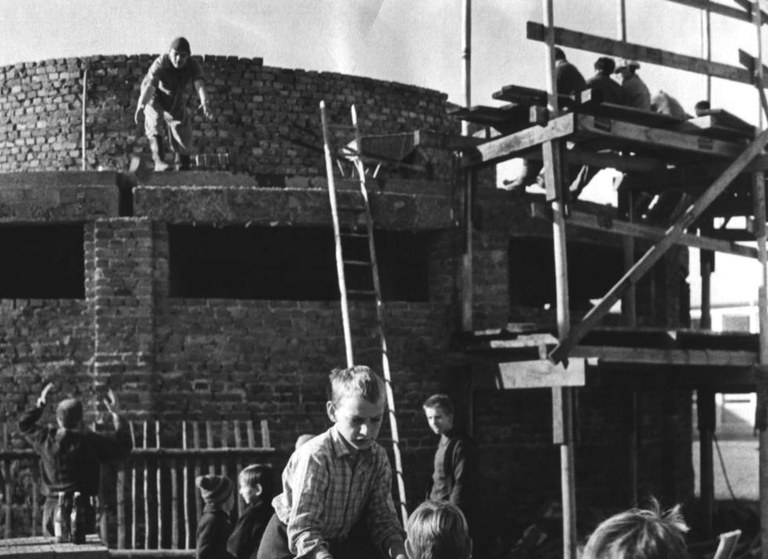 Kinder spielen vor einem im Bau befindlichen Backsteingebäude mit Gerüst und Leiter
