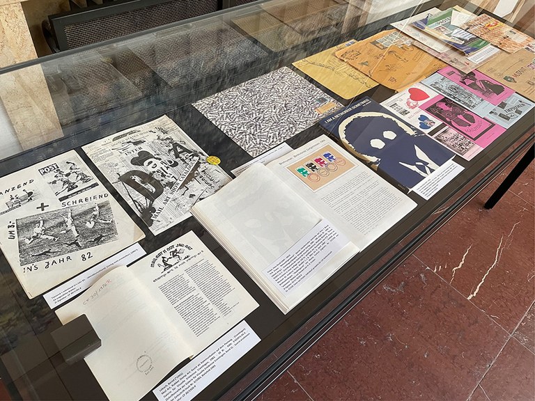 Gläserne Vitrine mit bunten Büchern drin. Bücher sind aufgeklappt.
