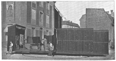 Schwarzweißfoto einer Straße. Vor einem Haus ist eine Konstruktion aufgebaut.