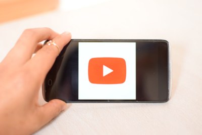 Eine Hand hält ein schwarzes Smartphone auf dem das rote YouTube-Icon erscheint.