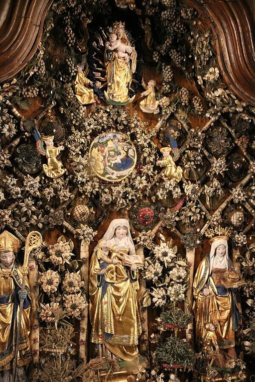 Hölzernes Reliquiar mit einigen Figuren und vielen floralen Elementen wie zum Beispiel Weintrauben. Die Figuren sind farblich gestaltet.